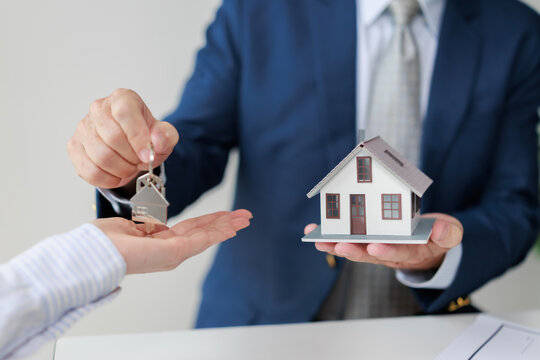 Real estate agent handing house keys and a model home to a client, symbolizing home ownership, property investment, and new beginnings