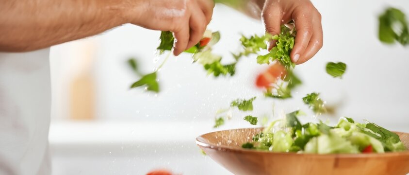 Chef tossing fresh salad ingredients into a wooden bowl with dynamic motion