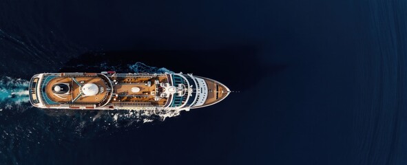 Aerial drone view of large cruise liner vessel sailing on deep blue sea water. This liner glides across calm ocean creating white foam wake. Ship sails on sunny day towards horizon.