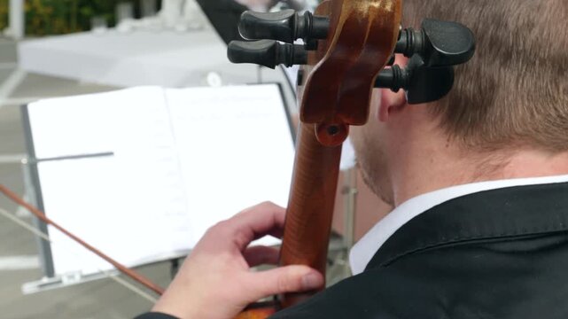Over the shoulder view of a musician playing cello with sheet music at a wedding ceremony
