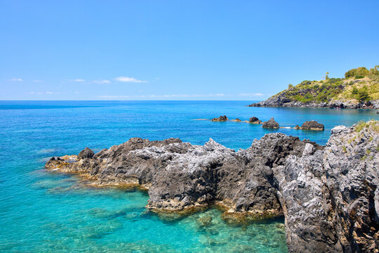 Scenic view of rocky coastline with clear turquoise sea water in Scalea, Calabria, Italy. Beautiful Mediterranean landscape under a blue sky.