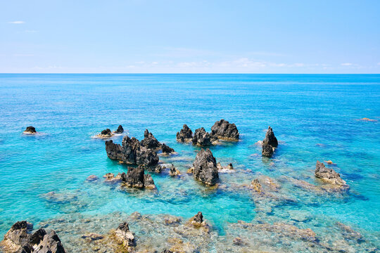 Dark volcanic rocks in crystal clear turquoise sea water in Scalea, Calabria, Italy. Scenic coastal Mediterranean landscape on a sunny summer day.