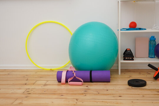 A collection of vibrant fitness gear including a yoga mat, exercise ball, and weights arranged in a home gym. Brightly colored equipment for a healthy lifestyle, pilates, or fitness training.