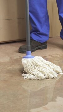 Male worker cleaning-up a slip hazard on the floor of an industrial plant with white mop.