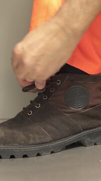 Close-up of a manufacturing worker's hands tying the laces on his work boots in a factory.