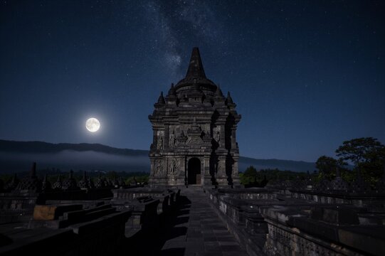 The central stupa of Borobudur Temple stands majestically at night in Central Java, Indonesia, under a clear sky with a full moon and Milky Way.