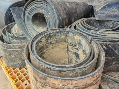 ​Used rubber conveyor belt rolls in industrial warehouse storage. Dirty heavy duty conveyor belts with mud stains for manufacturing, mining industry, recycling material, and waste management concept