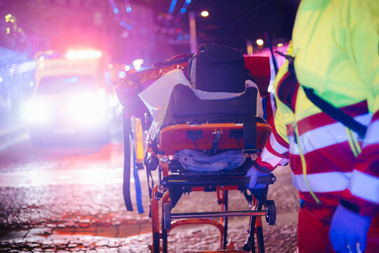 Paramedic pulling stretcher with medical equipment from emergency ambulance on city street at night. Emergency medicine, night shift, urgent care and healthcare concept.