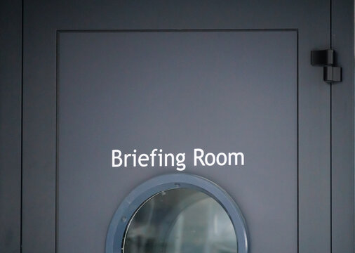 Door sign labeled "Briefing Room" at a professional event or corporate facility