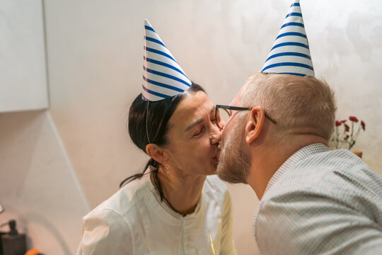 Couple Birthday Kiss Home: Celebrating anniversary indoors; a man and woman wearing party hats share a kiss at home, signifying love and celebration.
