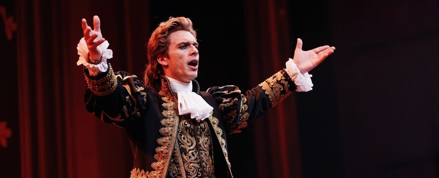 Male opera singer performs passionately on stage in ornate baroque costume. Dramatic gestures and vocalization captivate audience with powerful voice and grand performance artistry.