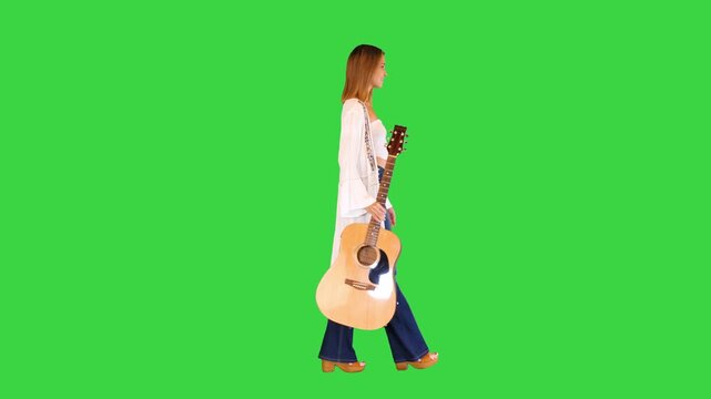 Beautiful young woman walking around with an acoustic guitar on a Green Screen, Chroma Key.