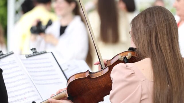 Close up of a female violinist playing violin with sheet music at an outdoor wedding ceremony