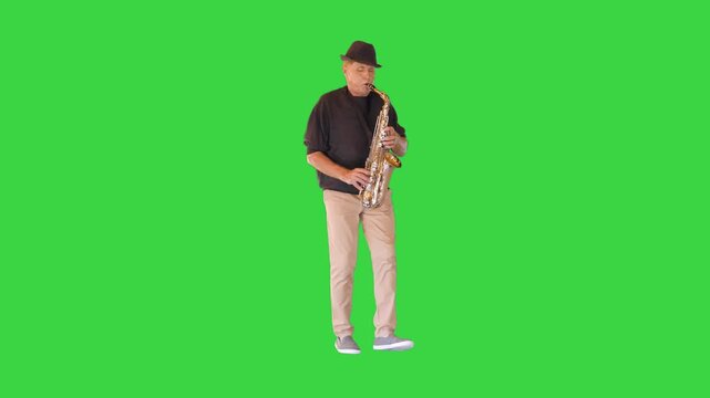 An elderly man walks in a funny manner playing the saxophone on a Green Screen, Chroma Key.