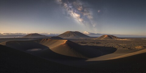 Fototapeta premium A panoramic view of volcanic cones under a starry sky at twilight in a barren desert environment captures the serene and majestic beauty of the Milky Way's galactic core.