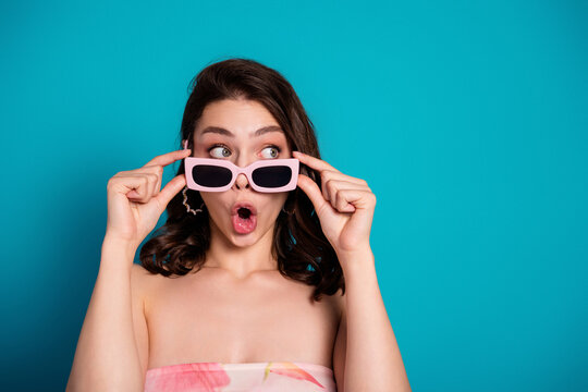 Surprised young woman in pink sunglasses and strapless floral top reacting with wide eyes against a turquoise background &mdash; playful summer fashion portrait with retro style