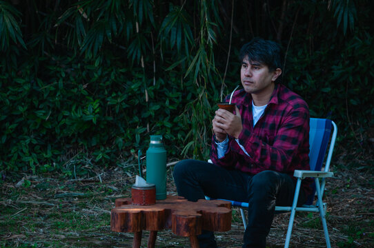 Hombre con camisa a cuadros sentado bebiendo mate, bebida caliente y contemplando el horizonte, momento de meditaci&oacute;n