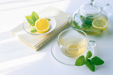 Fototapeta premium Book and fresh mint herbal tea with lemon on a bright table