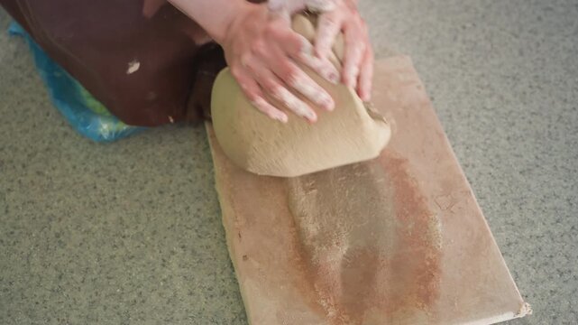 White woman potter centering clay hands, pressing and compressing mound on board in studio, closeup of palms and wrists shaping centered form, demonstration of rhythm, pressure and skilled hand