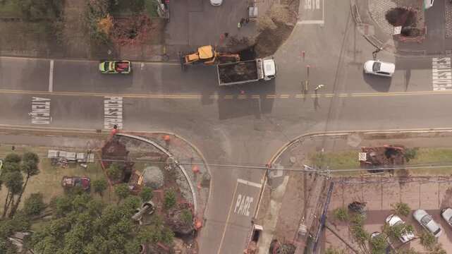 Drone footage descending over road construction excavator loading truck at city intersection