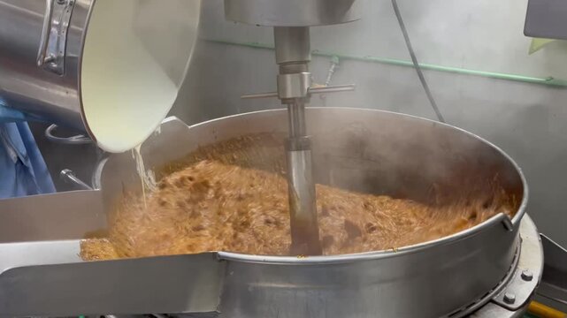 Caramel cooking process in industrial food production. Heated sugar mixture being cooked in a stainless steel kettle to develop color, flavor, and texture for food manufacturing applications.
