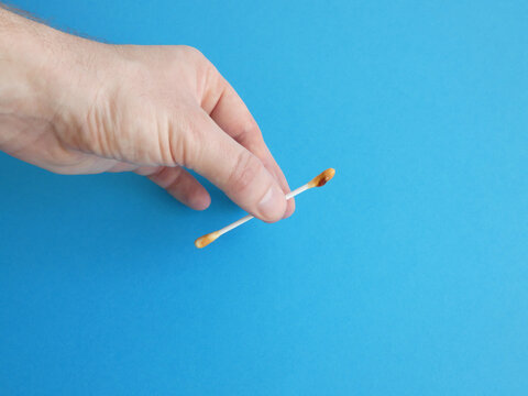Male fingers holding dirty cotton swab with earwax on blue background