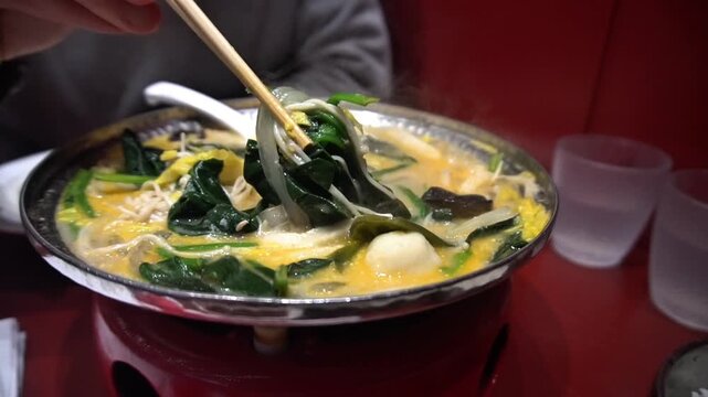 A man mixes Chinese soup with spinach, seaweed, and vegetables with chopsticks. Delicious hot Asian noodles with seafood for lunch