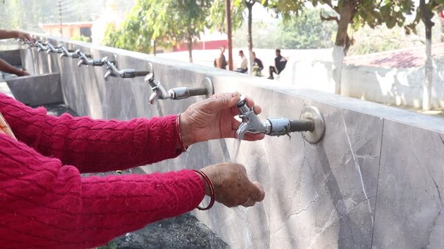 Raw video footage of a rural Indian woman washing hands under running water taps at a public washing area in Uttarakhand village showing hygiene and daily life.