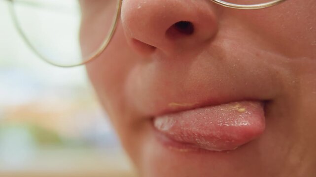 Closeup white woman licking lips, tiny cheese smear on upper lip, playful tongue flick, glasses reflection, satisfied expression, soft background blur, intimate texture study after bite