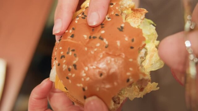 White office worker grabbing quick burger at desk overhead view of hands holding seeded bun beside coffee cup and tray, casual midday break with crumbs on tabletop and focused workplace energy