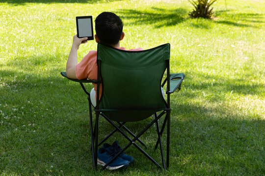 A young person reading an e-book in a folding chair in the park