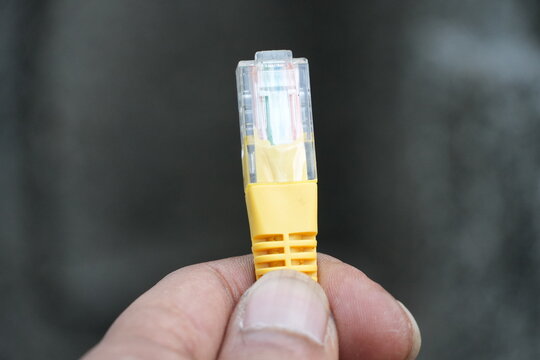 A person's hand holds a yellow Ethernet cable connector, showing the internal wiring and pins clearly.