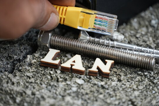 Wooden letters spell 'LAN' as a hand holds an Ethernet cable near a PoE injector.