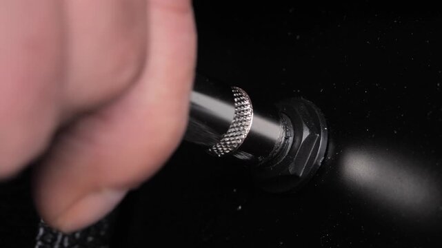 Close-up hand plugging guitar cable into black amplifier, musical preparation, equipment detail, performance atmosphere. music production concepts, rock culture visuals, musician lifestyle content