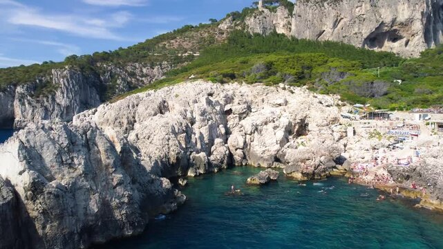 Wide drone panorama of Capri Faro beach showing swimmers and rocky coastline scenery