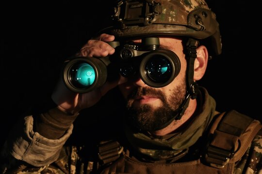 Man in military helmet wears night vision goggles, peering into darkness. Soldier uses advanced optics for reconnaissance, surveillance, or night operations. Focus on tech.