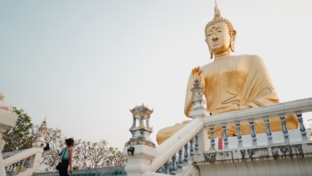 Traveler ascending temple steps, observing giant golden buddha statue
