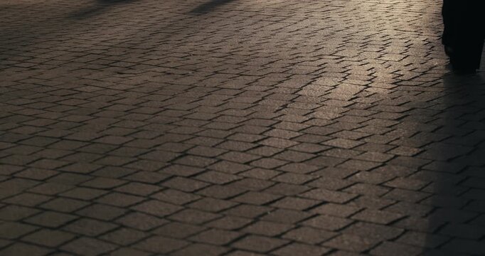People walking across a cobblestone street casting long shadows during sunset in Zagreb Croatia.