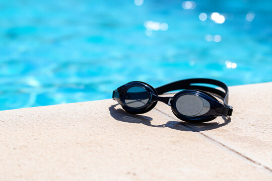Black Swimming Goggles Resting on Poolside with Clear Blue Water Background