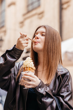 Young woman eating traditional Czech chimney cake with whipped cream on street in Prague