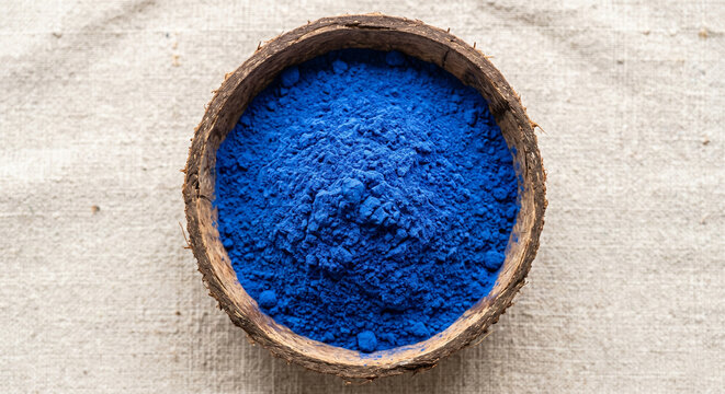 Vibrant blue spirulina superfood powder in natural coconut bowl on linen