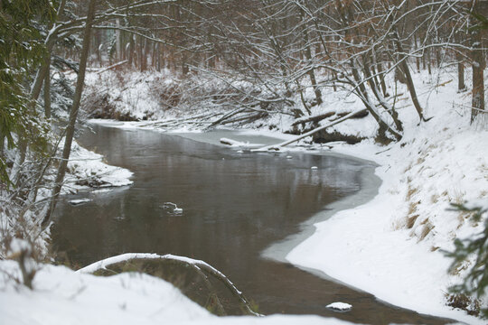 Malerischer Flusslauf im verschneiten Winterwald mit leichtem Eisgang