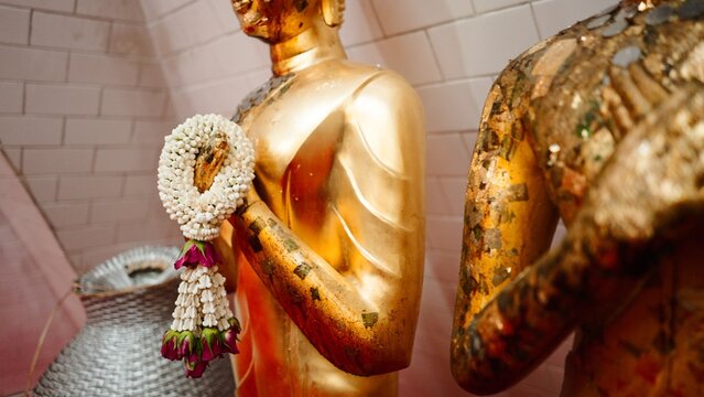 Golden buddha statue adorned with a jasmine garland in a thai temple