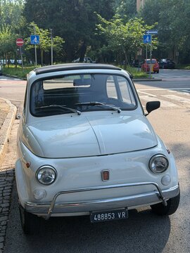 Classic White Fiat 500 Parked on European Street: A vintage white Fiat 500, a beloved icon of Italian design, is parked curbside on a sun-drenched street.