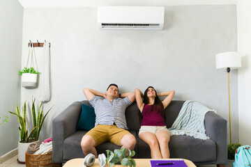 Plakat Relaxed couple sitting at home with air conditioning on hot summer day, enjoying cool air and comfort