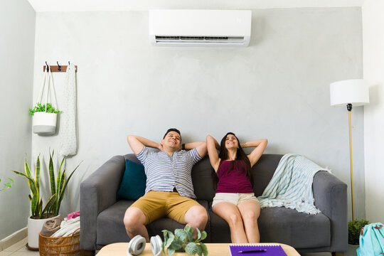 Relaxed couple sitting at home with air conditioning on hot summer day, enjoying cool air and comfort