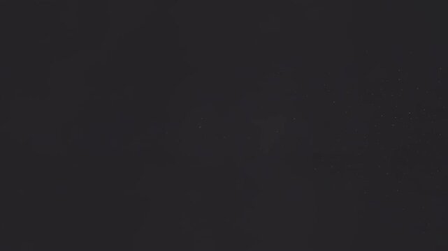Glowing golden sparks drift slowly through the dark atmosphere in this elegant motion video footage featuring a bright light source emitting particles across a deep black textured and cinematic backgr