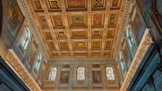 A stunning interior view of the Basilica of Saint Paul Outside the Walls in Rome, Italy, featuring rows of majestic marble columns and a magnificent gilded coffered ceiling.
