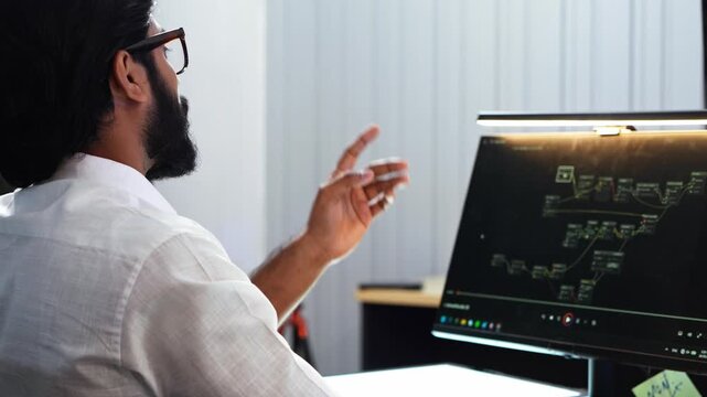 Software engineer wearing glasses pointing finger at computer monitor screen displaying node editor system workflow diagram during tech project development in office workspace