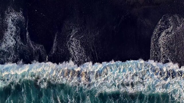 Aerial looking down at waves on a black sand beach in Bali Indonesia.